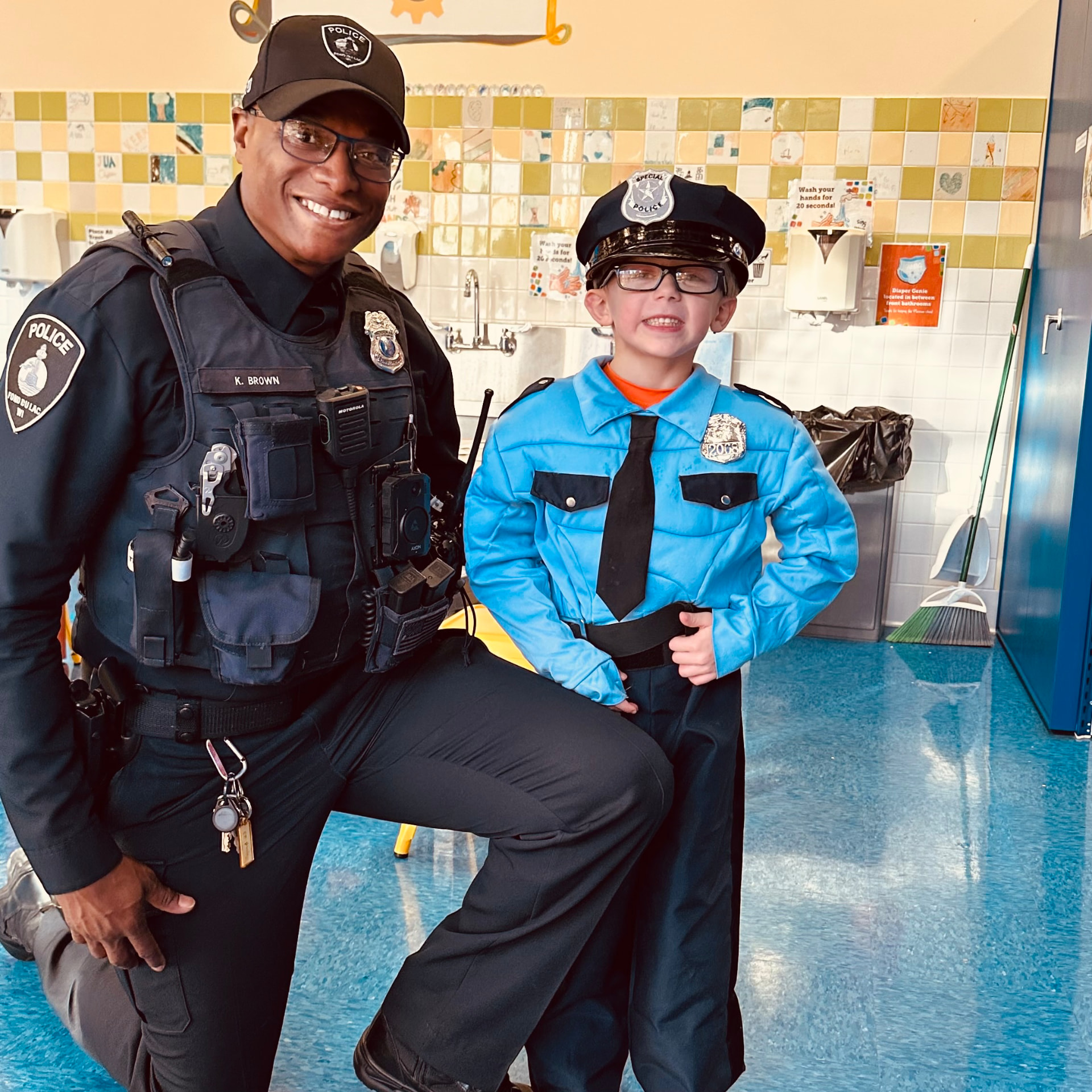Officer Keywon Brown kneeling with a young child dressed in a play police uniform.