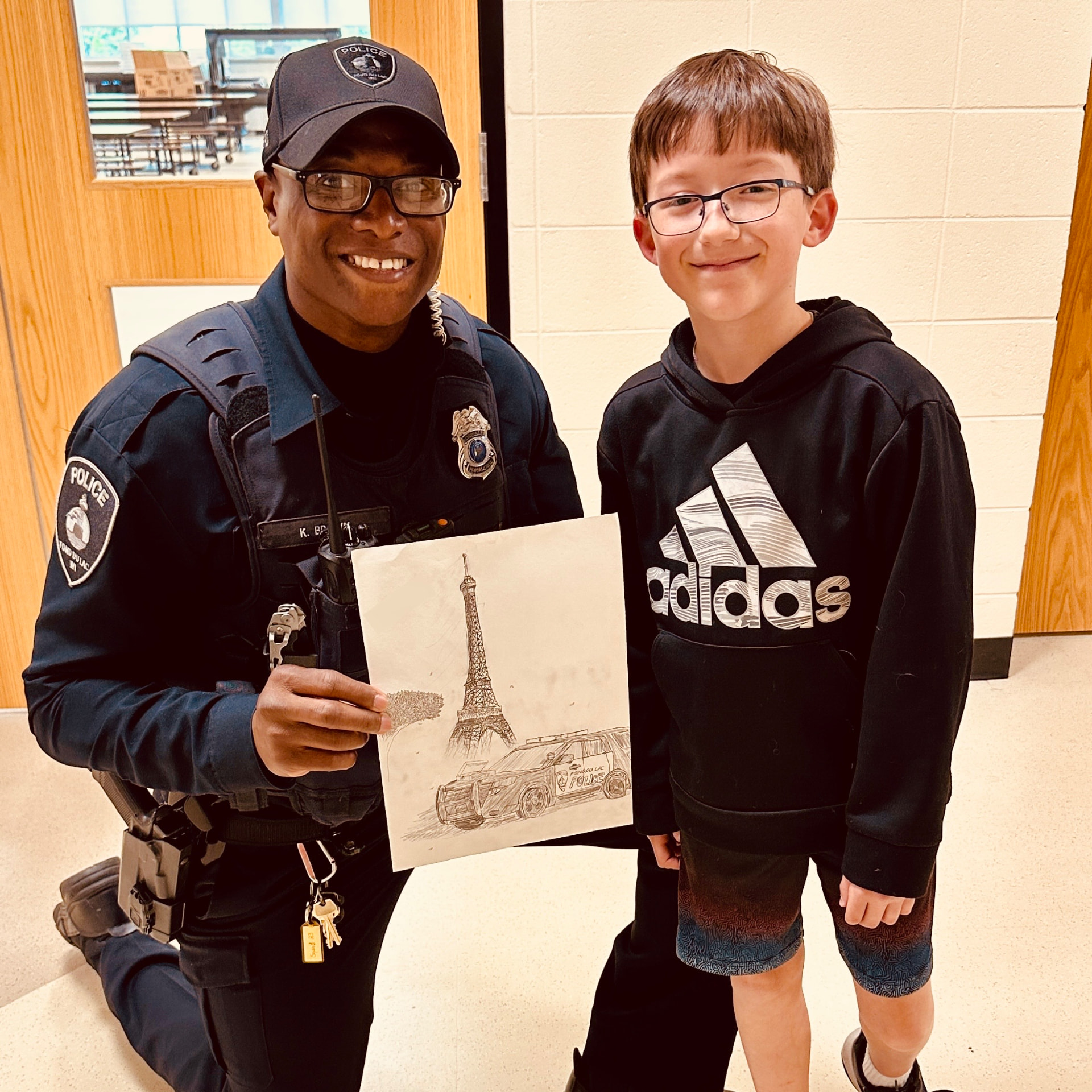 Officer Keywon Brown kneeling beside a student holding a drawing of a police squad car.