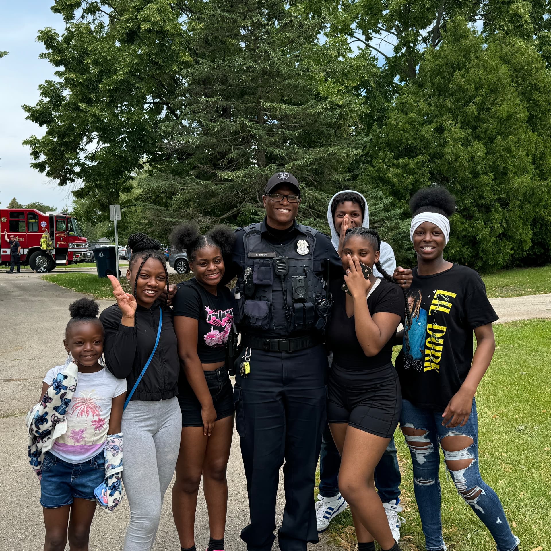 Officer Keywon Brown in uniform posing with a group of children and teenagers near a Fond du Lac Fire and Rescue truck.
