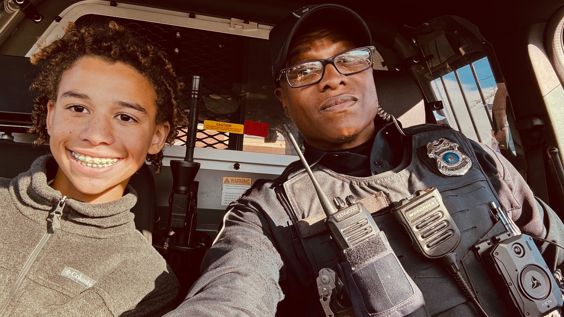 Officer Keywon Brown seated in his squad car with a smiling middle school student.