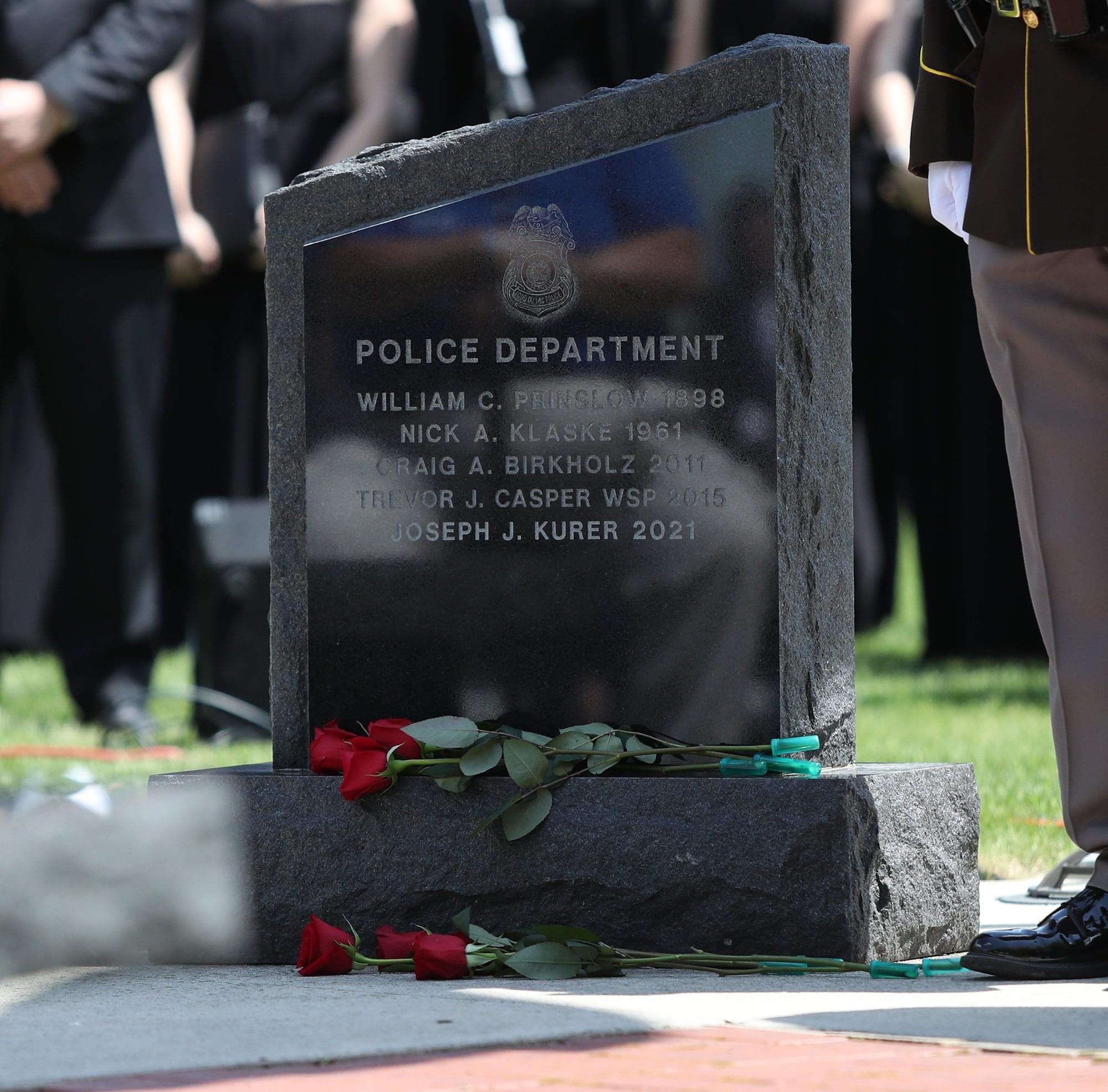 Fond du Lac Police Department memorial monument engraved with the names of fallen officers, including Officer Craig A. Birkholz, Badge 67, with red roses laid at its base.